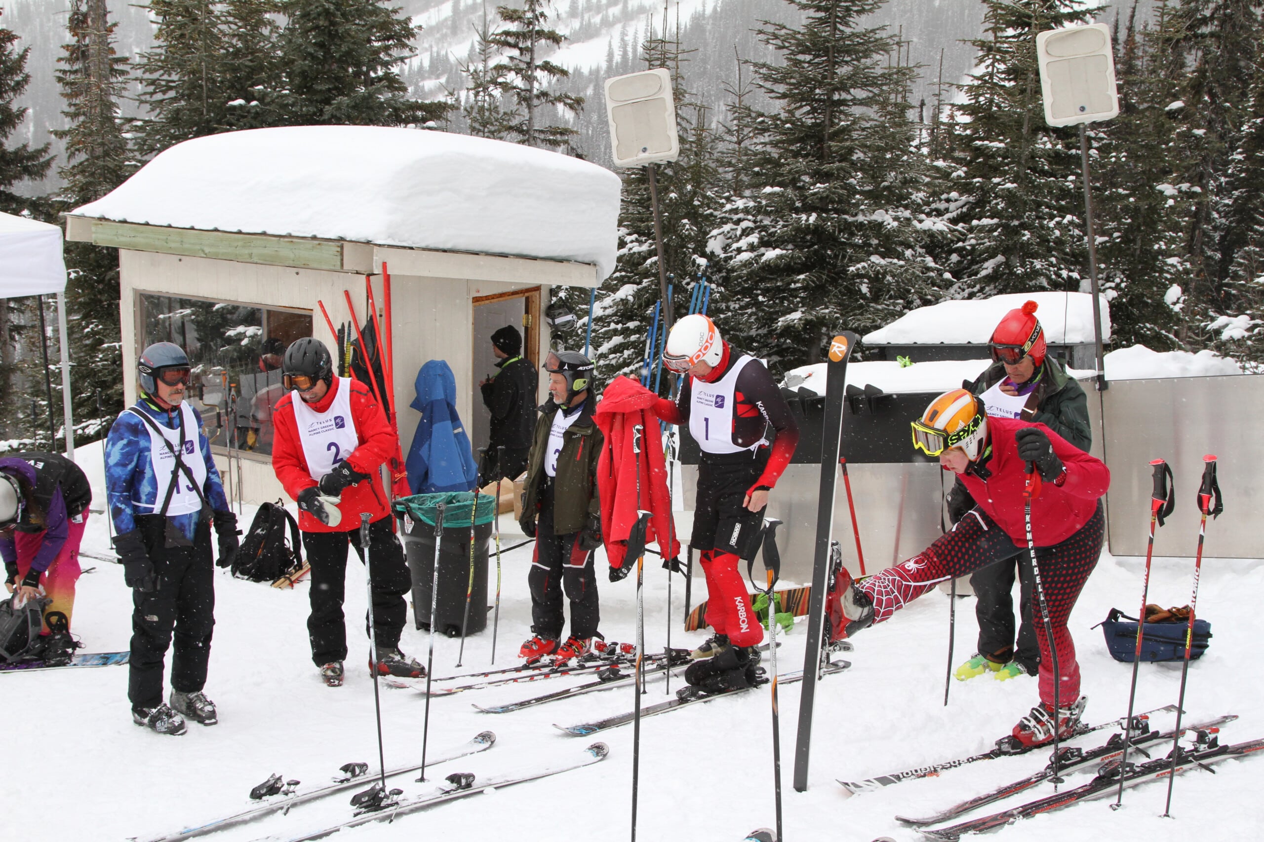 People wear red spandex ski racing clothes while standing outside in the snow before racing in competition.