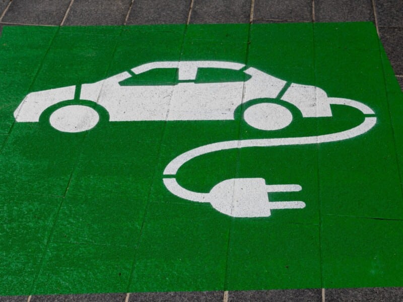 A white car is painted on a green background on the ground. A plug is attached to the car to indicate it is electric.
