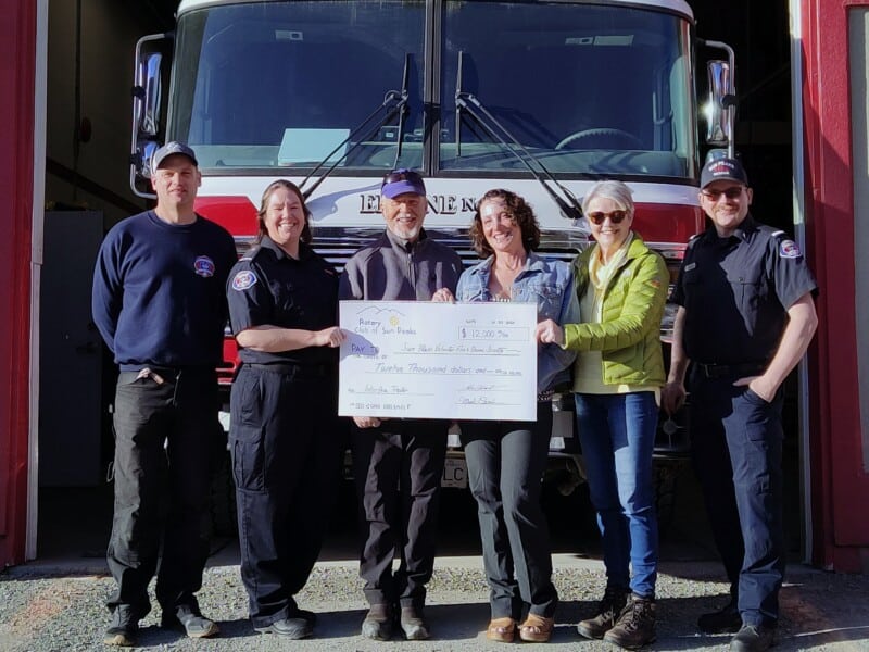 Members of Sun Peaks Rotary Club members and Sun Peaks Volunteer Fire and Rescue Society stand in front of a fire truck on a sunny day holding a giant cheque.