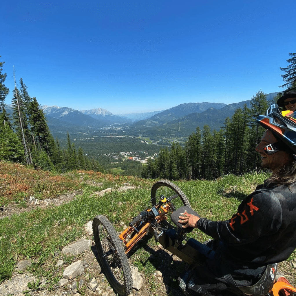 A man on an adapted mountain bike for Sun Peaks Adaptive sports views out to a vista with mountains and trees. 