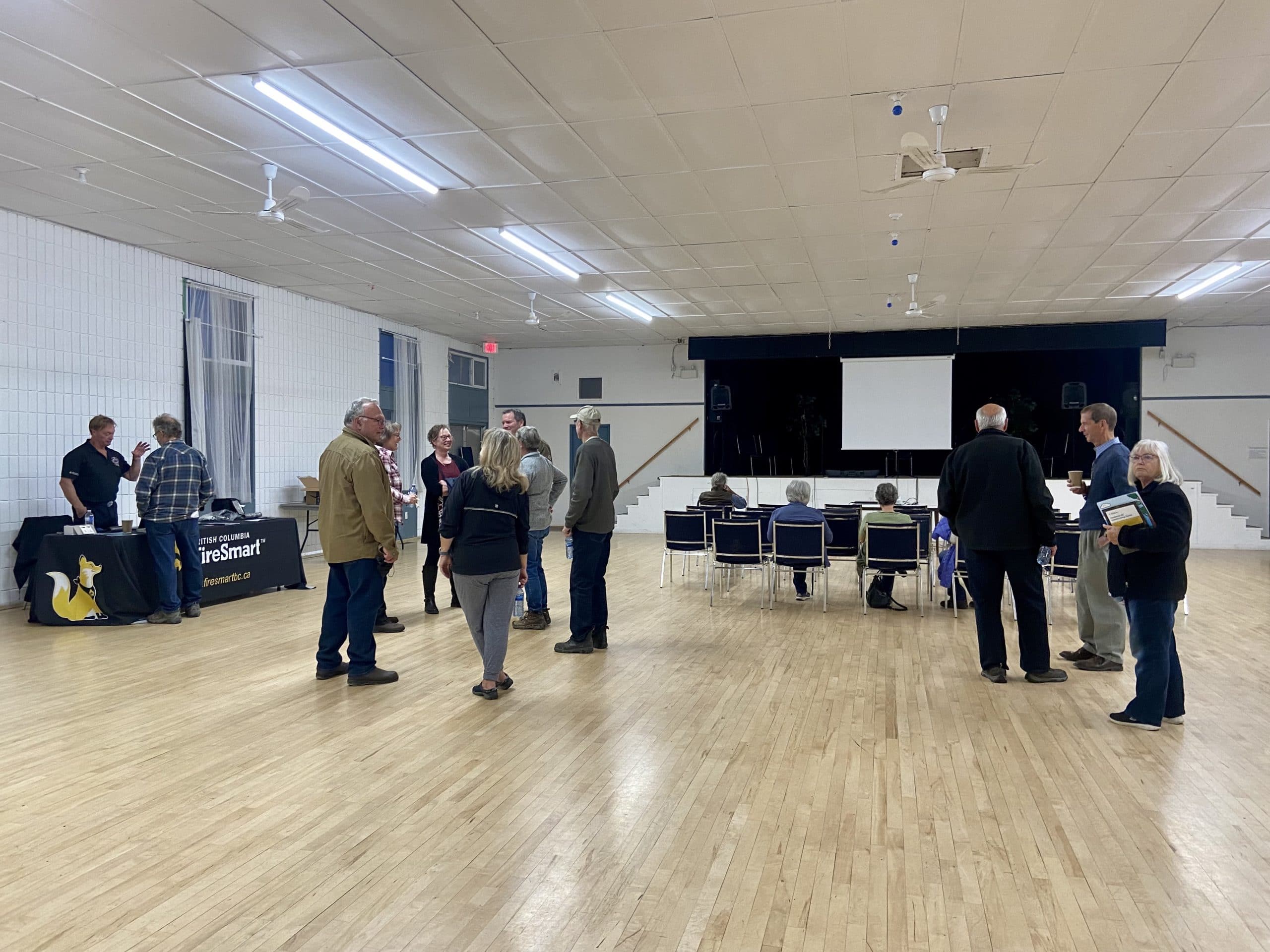 Around 15 people gather in small groups having conversations in a community meeting hall. 