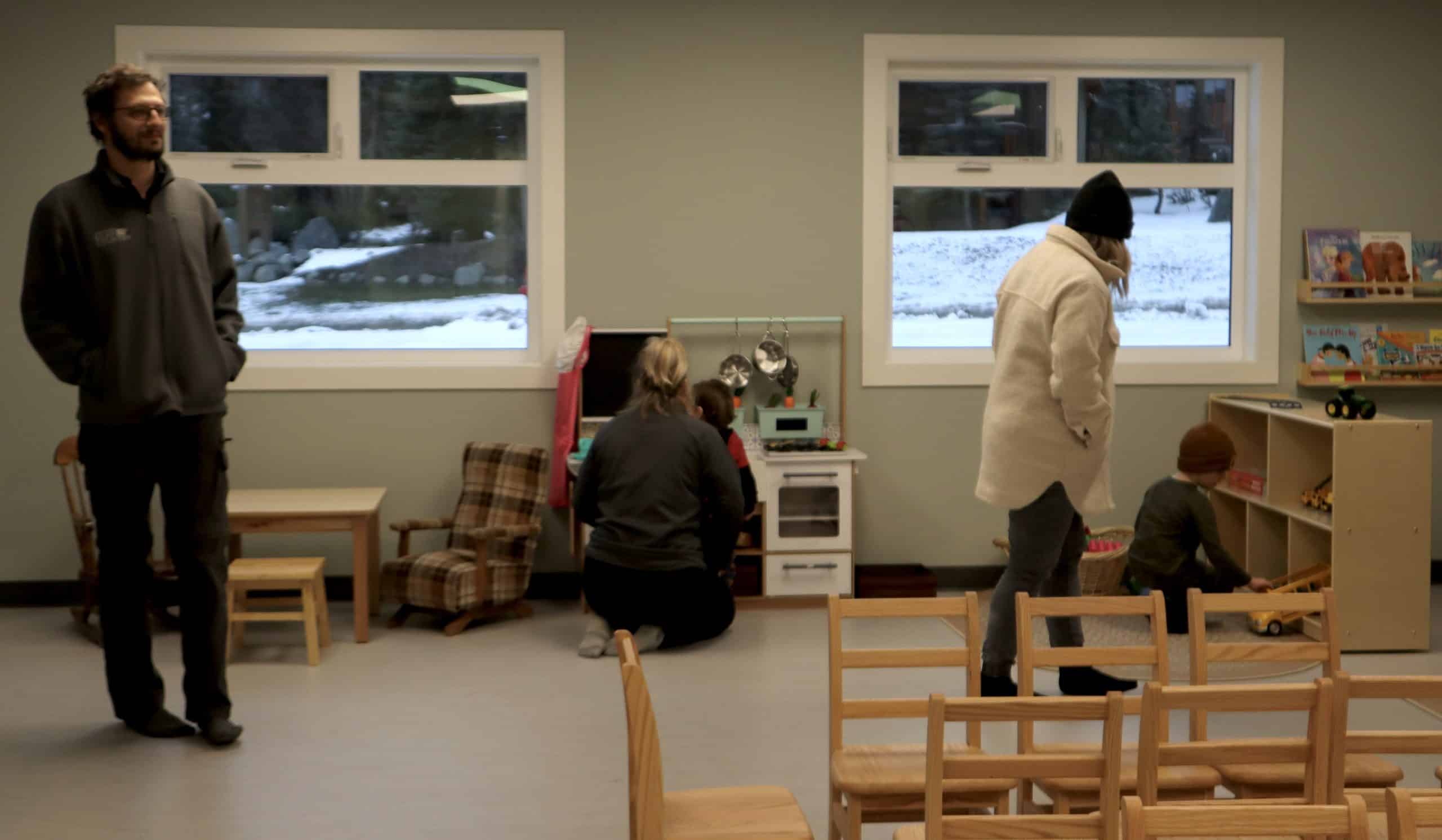 Adults and children inside the new daycare. Kids play with toys.