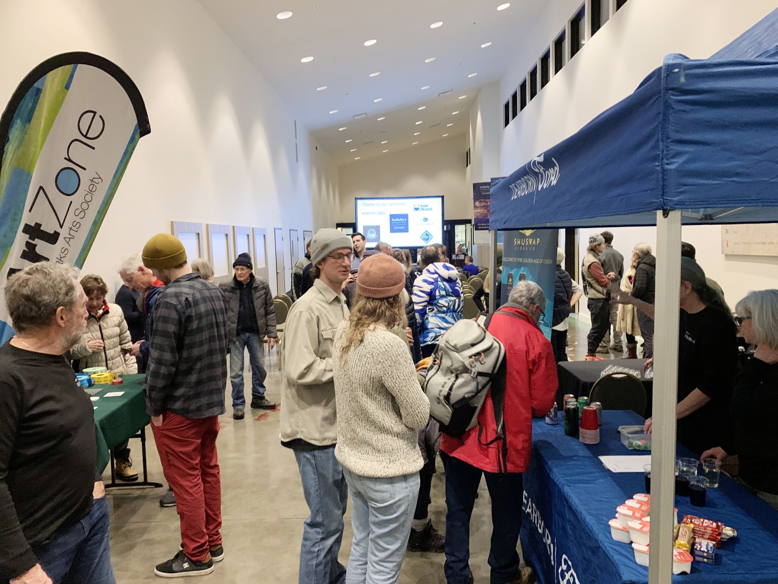 People gather indoors in a white room looking at vendor offerings.