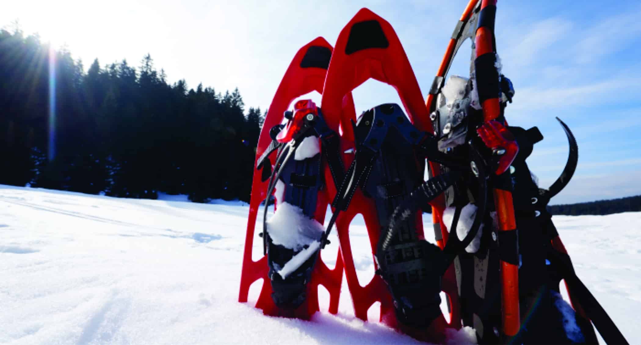 Red snowshoes are in snow outside with a blue sky in the background.