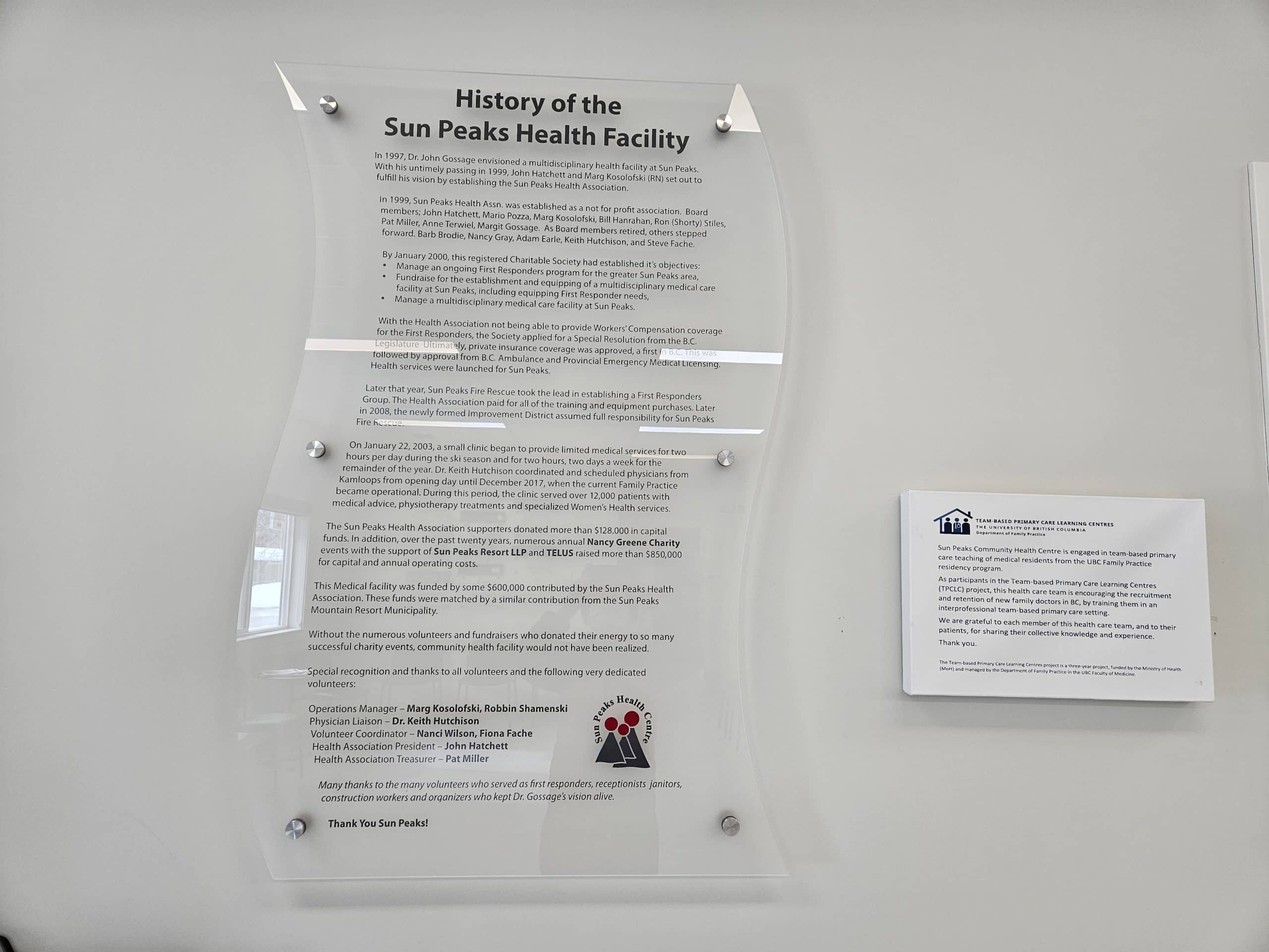A mounted on a beige wall plaque describes the history of Sun Peaks Health Association.