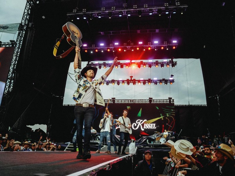 Brett Kissel holds his guitar over his head at a concert, brining the energy.