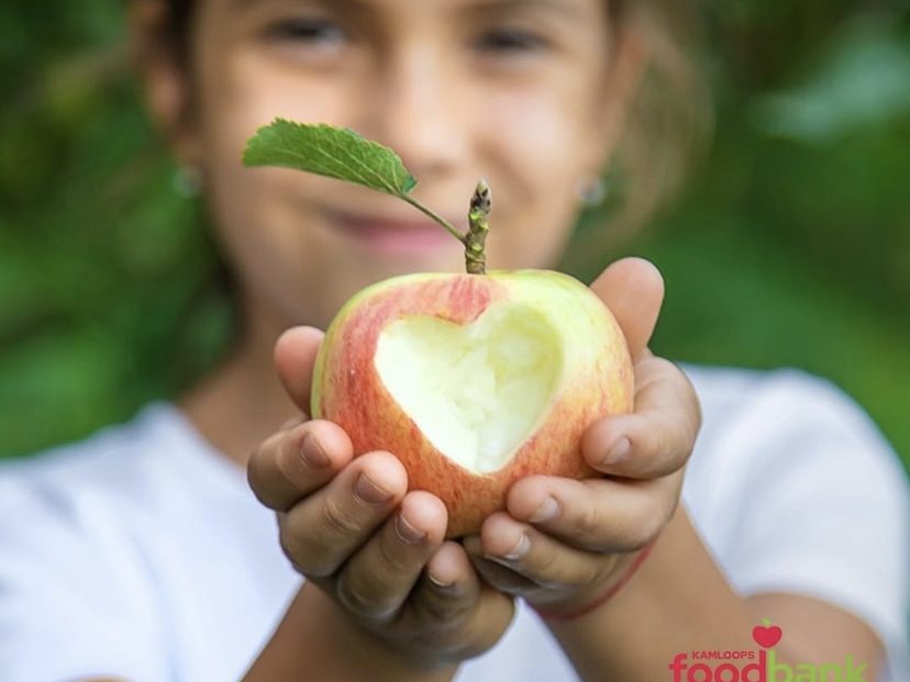 Kamloops Food Bank's feature image: a smile on a girl's face as she holds out an apple with a heart bitten into it.